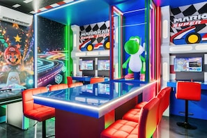 Ein auf Mario basierender Gaming-Raum mit mehreren Spielestationen, einem großen Bildschirm und lebhaftem Dekor.