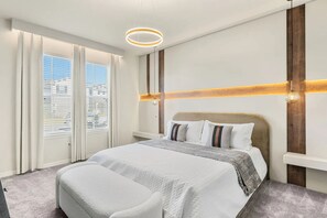A hotel room with a large bed, a view of the city through the window, and a modern light fixture. - Luxury 10br w/ Pool, Theater & Game Room (Clermont)
