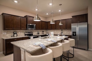 A modern kitchen with dark wooden cabinets, a stainless steel refrigerator, a granite countertop, and pendant lighting. - 10br Windsor Cay Resort Home + Private Pool (Clermont)