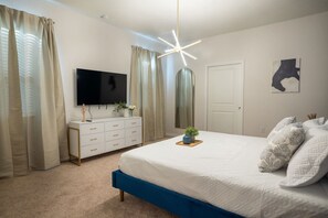 Un dormitorio con una cama, un aparador, un televisor, un espejo y una lámpara en el techo.