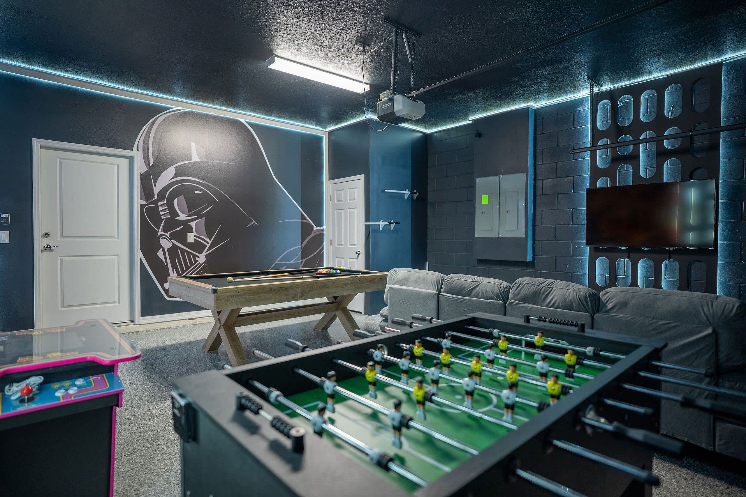 A room with a foosball table, a pool table, and a large mural on the wall.