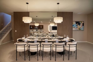 A dining area with a large round table, white chairs, and pendant lights. - 10br Windsor Cay Resort Home + Private Pool (Clermont)