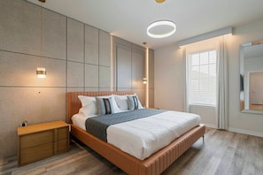 A modern bedroom with a wooden bed, bedside tables, a large window with blinds, and a wall-mounted TV. - 10br Home w/ Pool & Disney Themes (Clermont)