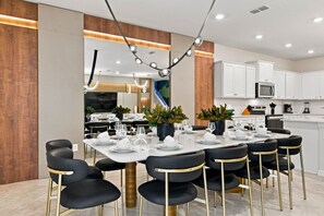 Un espace de salle à manger moderne, avec une longue table dressée pour un repas, entourée de chaises noires aux pieds dorés.