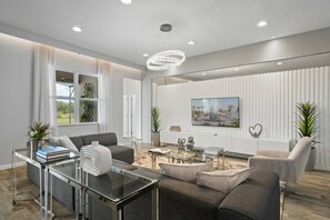 A modern living room with a glass coffee table, grey sofas, and a large painting on the wall. - Solterra 12 BDR 10 Suites 29 Guests Pool/spa (Davenport)