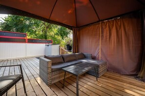 An outdoor patio with a covered seating area, a table, and a view of a fenced yard. - Little Red | Hot Tub | Fire Pit | Waskasoo | Yard (Red Deer)