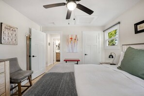 Ein Schlafzimmer mit einem Bett, einem Schreibtisch, einem Stuhl, einem Deckenventilator und einem Fenster.