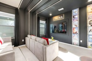 A modern living room with a sofa, a television mounted on the wall, and a cinema-themed decor. - 12br Home at Paradiso Grande, Near Disney (Orlando)