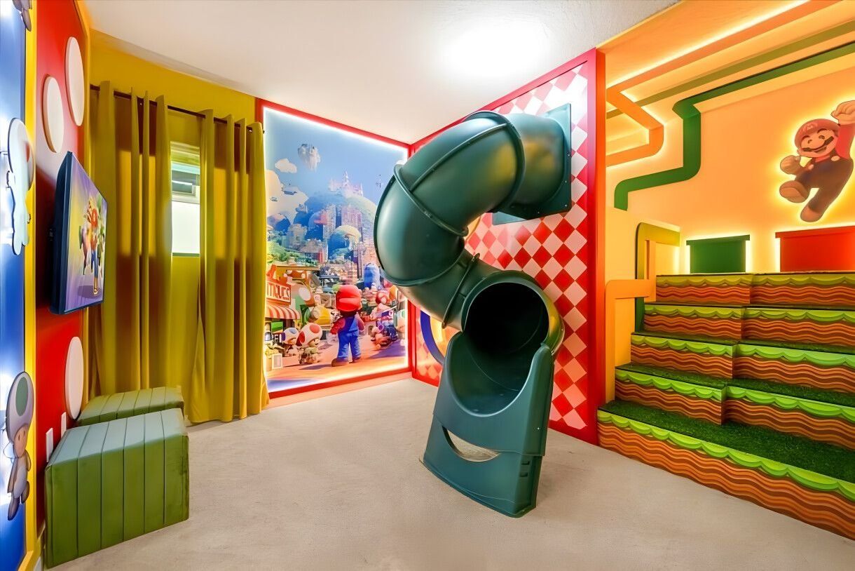 A colorful play area with a slide, a window with curtains, and a cartoon character on the wall.