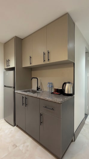 Une cuisine moderne avec des meubles gris, un réfrigérateur en acier inoxydable, un plan de travail en granit et une bouilloire.