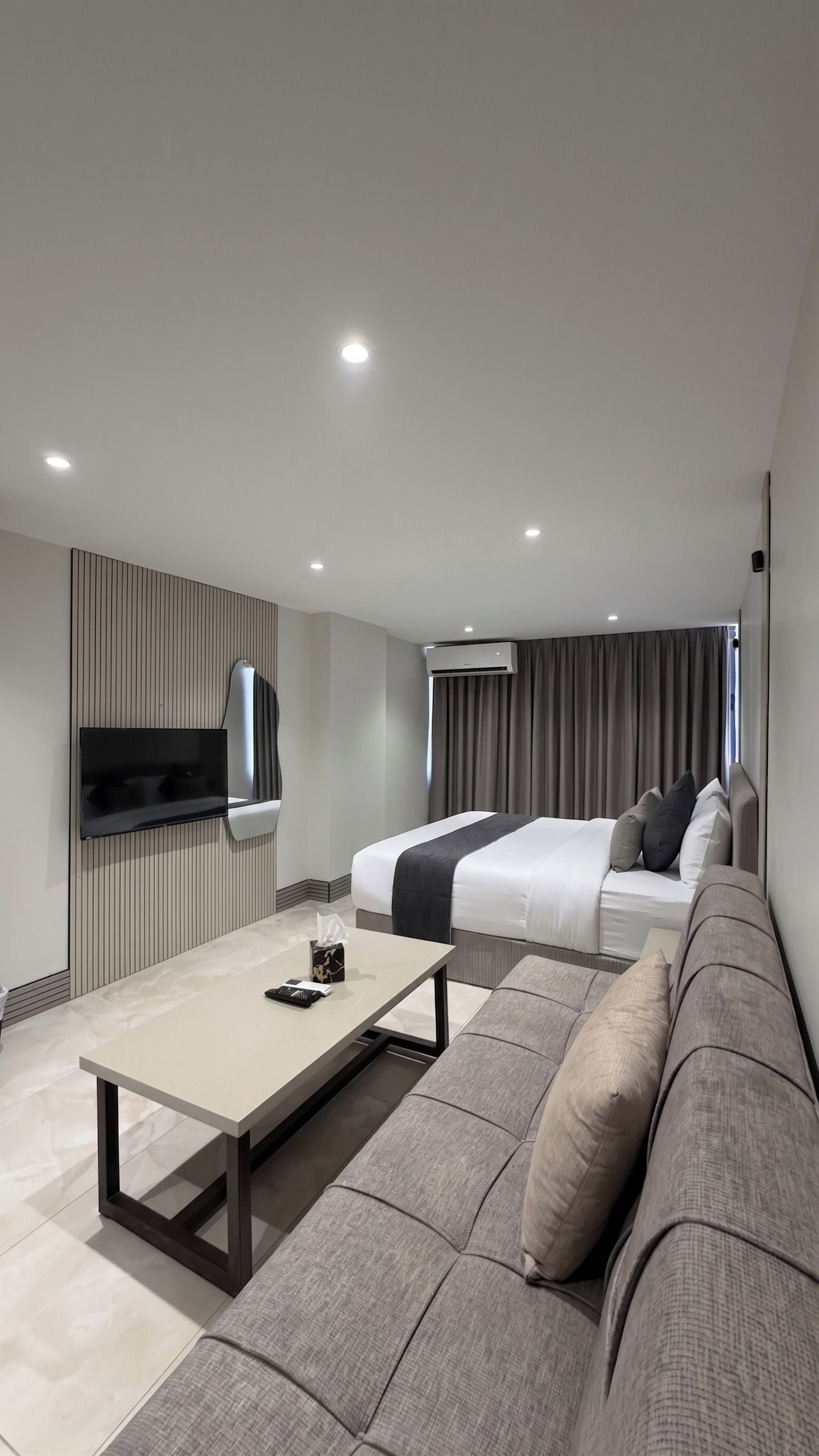 A modern hotel room with a flat-screen TV, a sofa, a bed, and a bedside table.