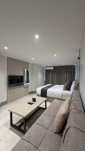 A modern hotel room with a flat-screen TV, a sofa, a bed, and a bedside table. - Azure Hotel (Aqaba)