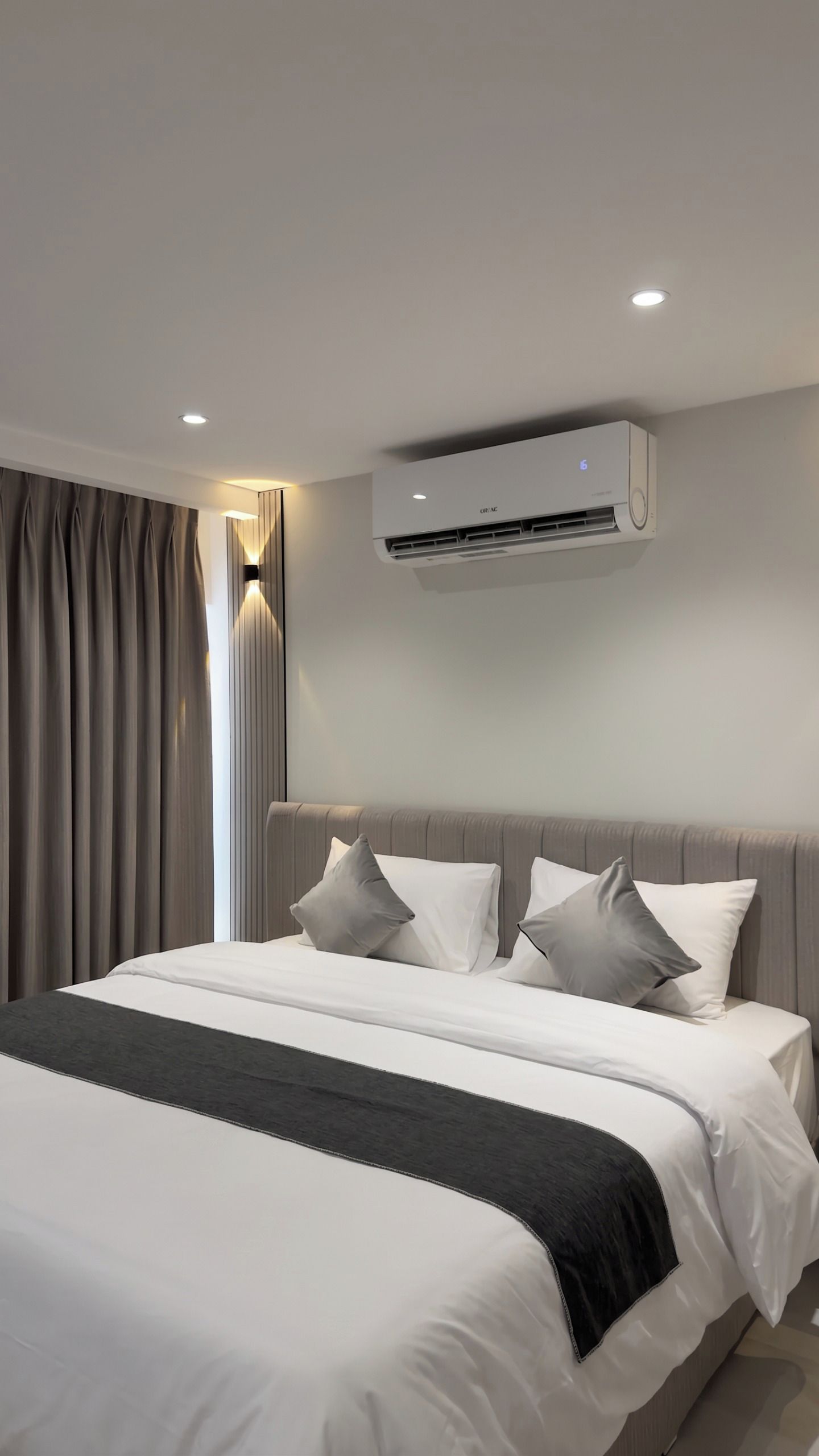 Et moderne hotelværelse med en stor seng, grå gardiner og en vægmonteret aircondition.