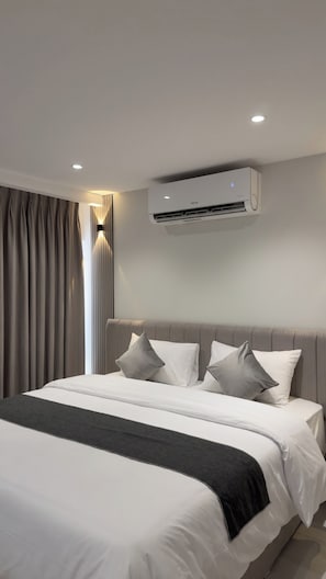 Une chambre d’hôtel moderne avec un grand lit, des rideaux gris et un climatiseur fixé au mur.