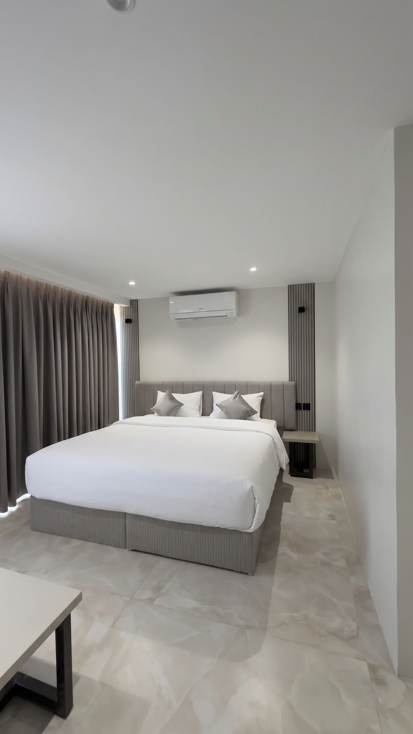 Habitación de hotel moderna con una cama grande, mesitas de noche, equipo de aire acondicionado y vistas al exterior.
