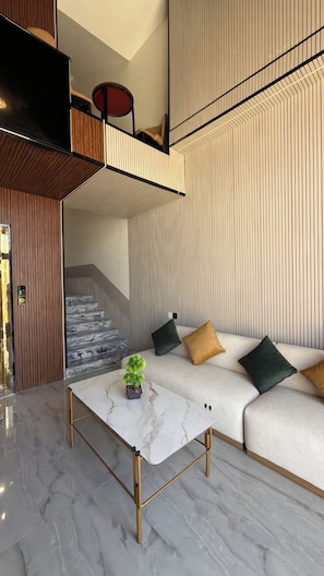 Un salon moderne avec une table basse en marbre, un canapé avec des coussins, un escalier et un mur en bois orné de lignes verticales.