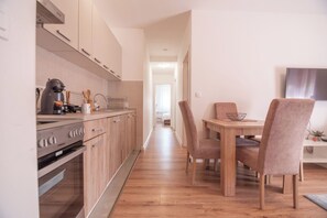 Een moderne keuken met houten kasten, een ingebouwde oven en een eethoek met een houten tafel en stoelen.