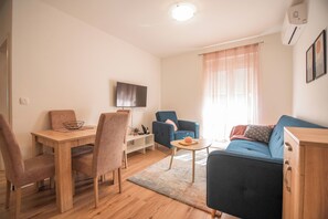 Een moderne woonkamer met een eetgedeelte, een flatscreen televisie aan de muur en een blauwe bank.
