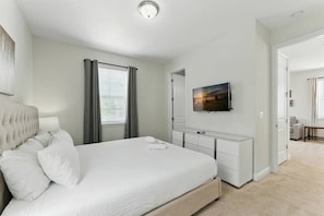 Une chambre à coucher comprenant un lit, une table de chevet, un miroir, une télévision et une porte donnant sur une autre pièce.