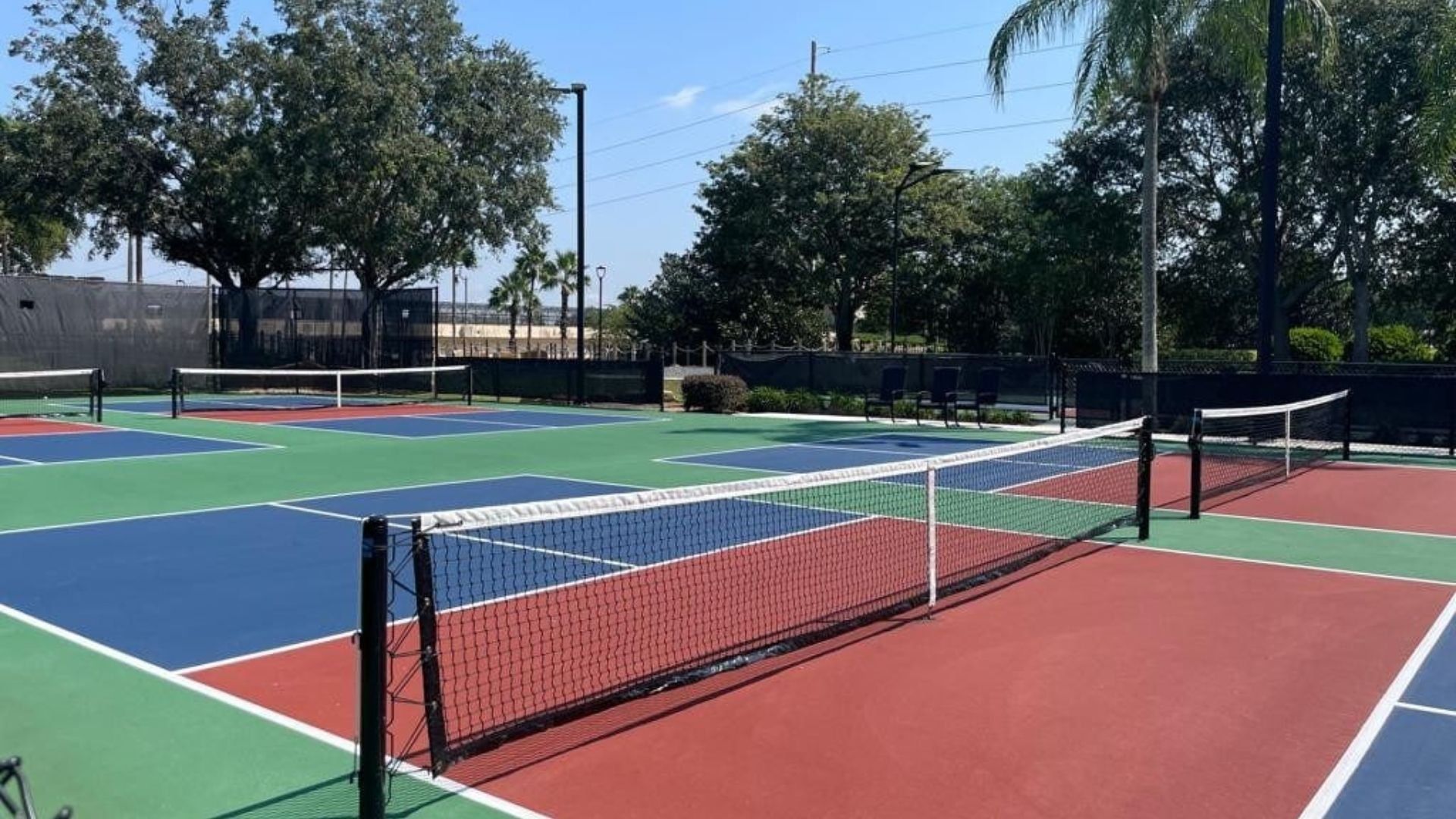 A tennis court with multiple courts, a net, and surrounding trees.