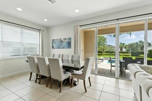 A dining area with a table and chairs, a painting on the wall, and a view of the outdoors through a sliding glass door. - 5-bedroom House With Pool and spa Near Disney (Kissimmee)