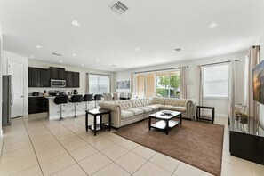 A modern living space with a kitchen, a sofa set, and a dining area. - 5-bedroom House With Pool and spa Near Disney (Kissimmee)