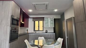 A modern kitchen with a central island, stainless steel appliances, and a dining area with white chairs.
