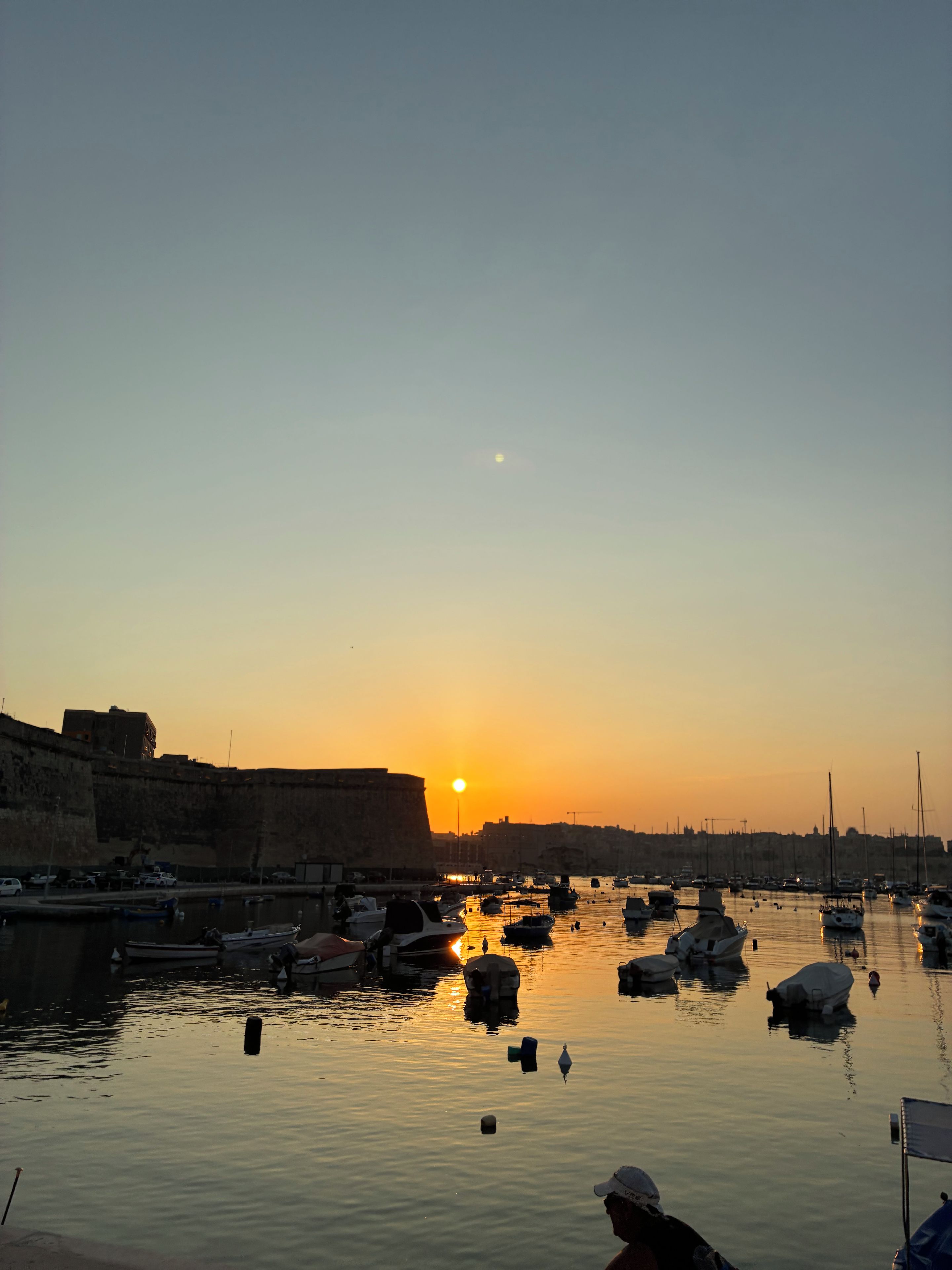 A harbor at sunset with boats and a large building on the left.