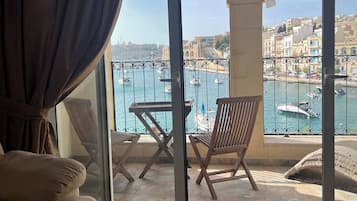 A balcony with a view of a harbor, a table, two chairs, and a sofa.