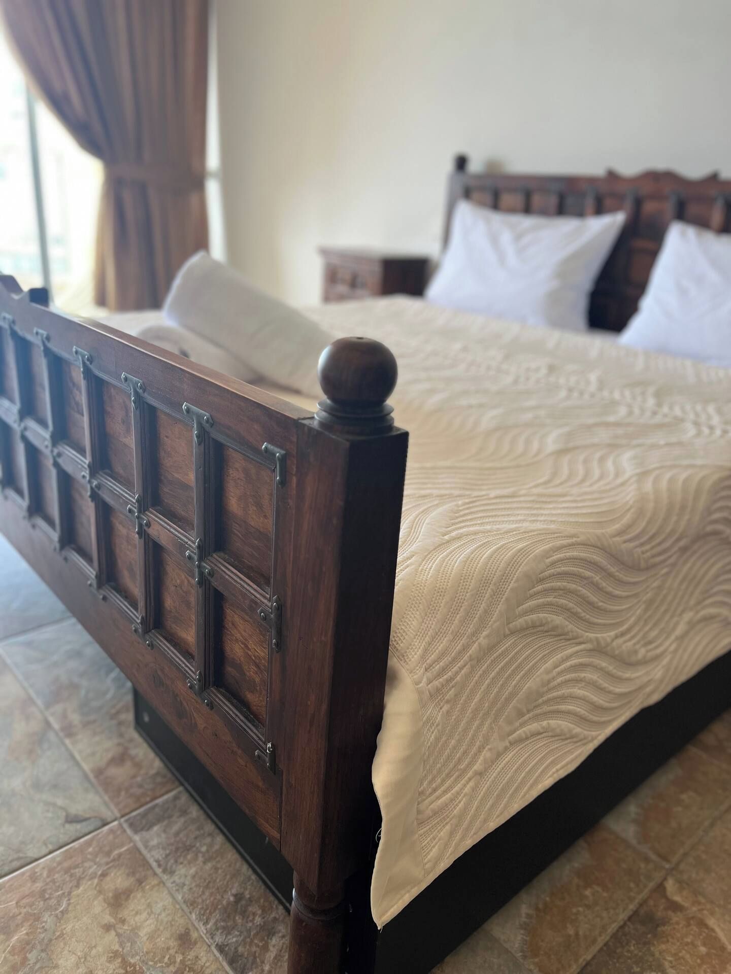 A wooden bed with a headboard, a patterned bedspread, and a nightstand with a lamp.