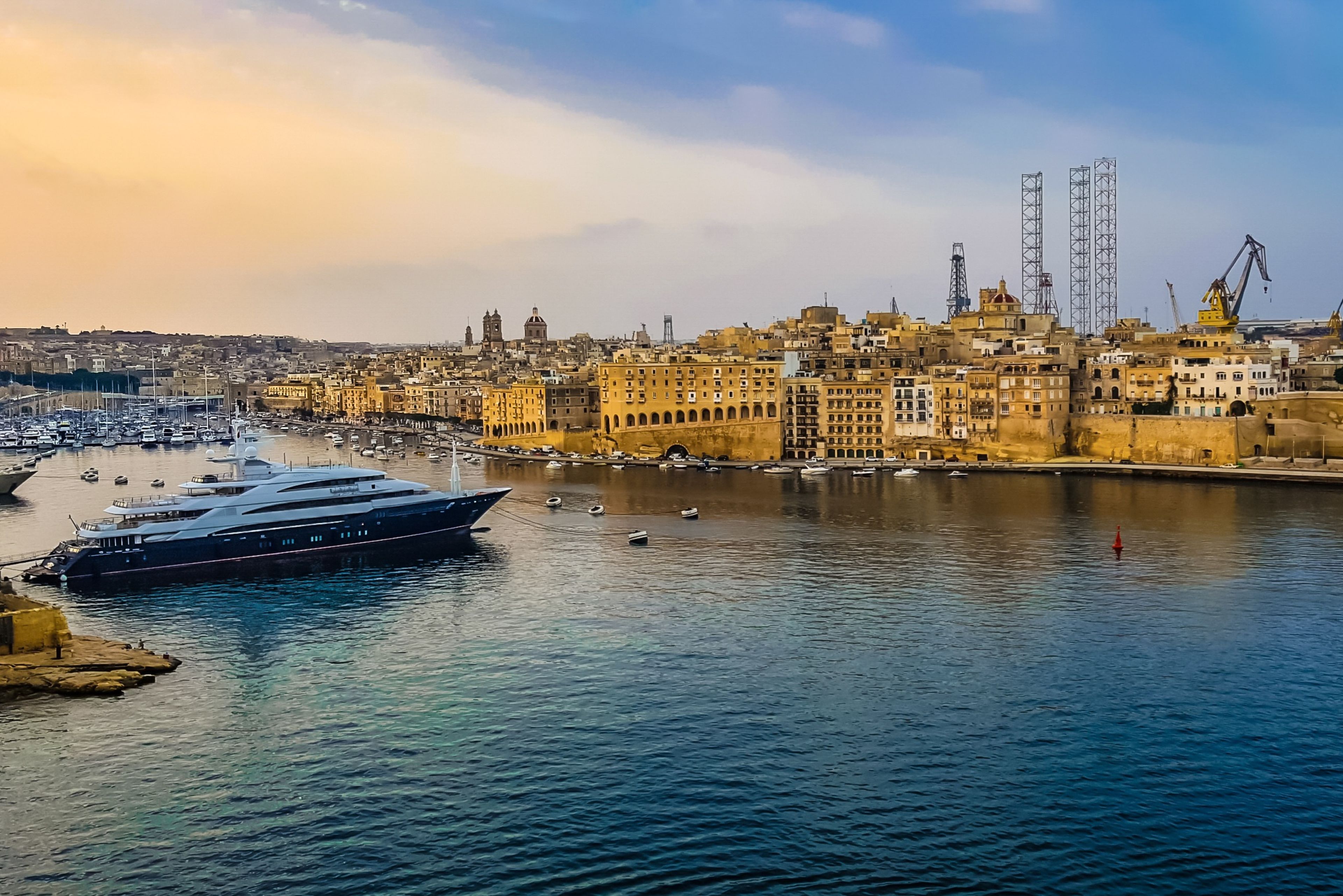 A large yacht docked at a marina with a cityscape in the background.