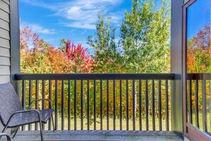 Ein Balkon mit Blick auf Bäume in Herbstfarben, einem Holgitter und einem Stuhl.