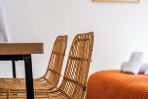 Ein Korbstuhl mit schwarzem Gestell, ein Holztisch und ein orangefarbenes Kissen.