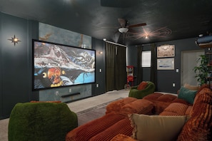 Ein modernes Wohnzimmer mit großem Flachbildfernseher, bequemen Sitzmöglichkeiten und einem Deckenventilator.