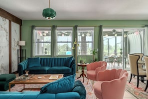A living room with a teal sofa, a coffee table, and a pink chair. There are windows with curtains and a ceiling fan. - Private Pool & Hot Tub, Game Room Near Disney (Davenport)