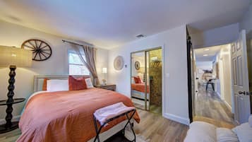 A bedroom with a bed, bedside table, lamp, and a view of a bathroom through a sliding door.