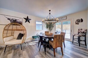 A dining area with a round table, wicker chairs, and a hanging light fixture.