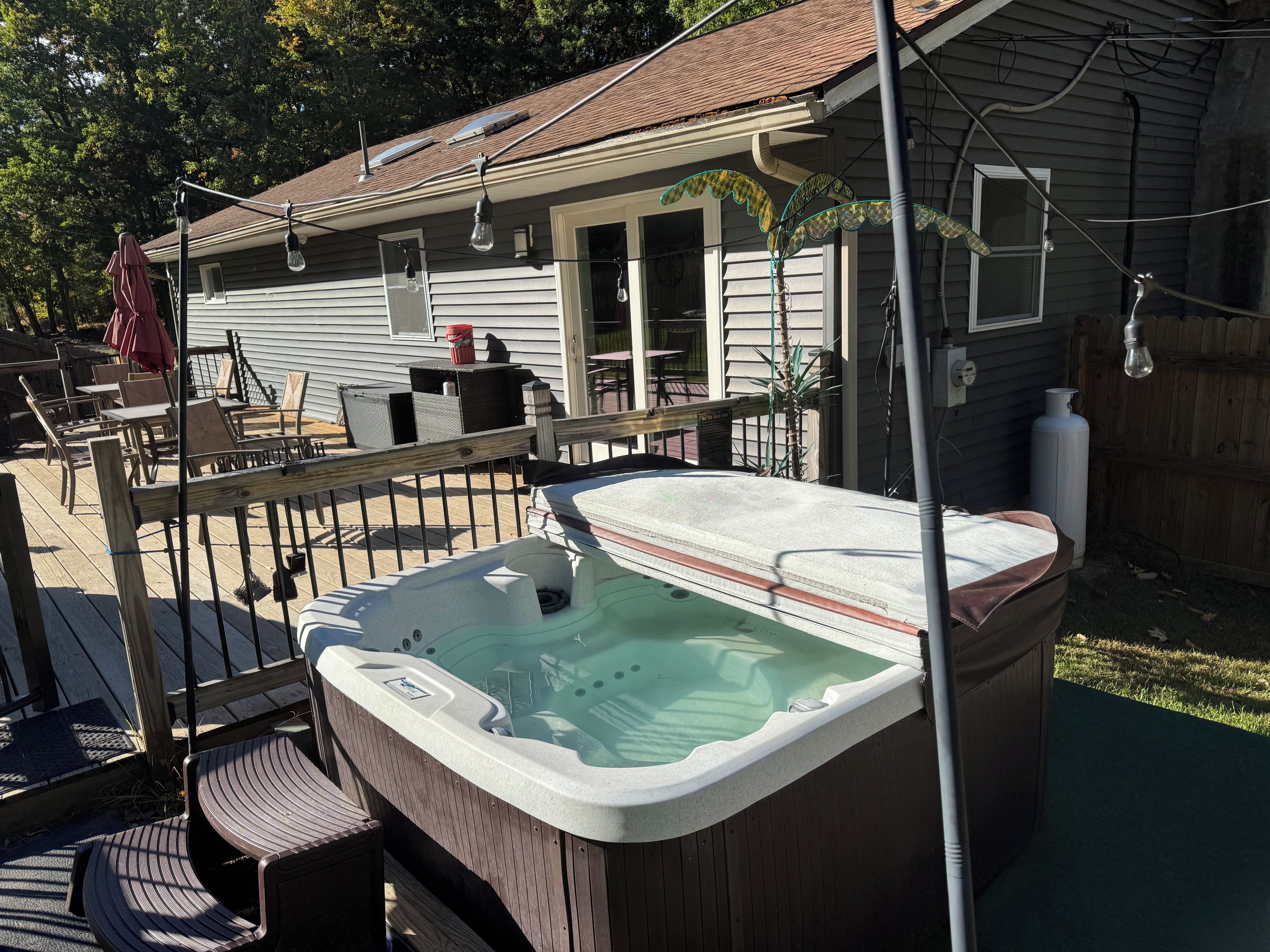 A hot tub in a backyard with a wooden deck, outdoor furniture, and a house in the background.
