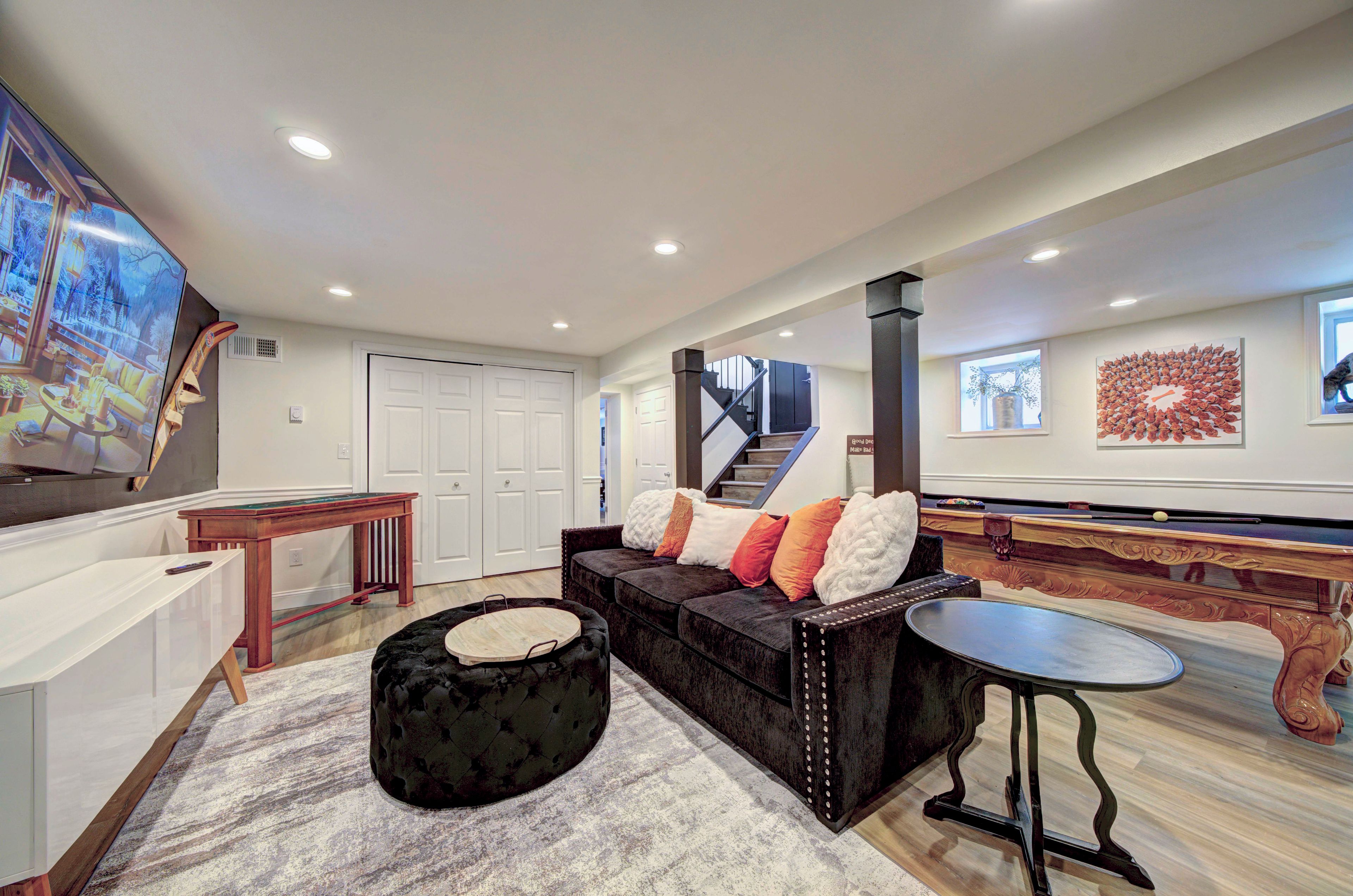 A modern living room with a sofa, ottoman, and a flat-screen TV.