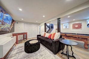 A modern living room with a sofa, ottoman, and a flat-screen TV. - Spacious Private Home 1 Bedroom Getaway with Hot Tub Game Room and Bar (Tafton)