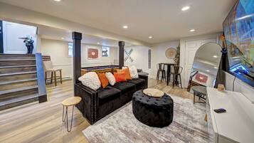 A modern living room with a black sofa, a round ottoman, and a pool table.