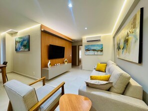 A modern living room with a flat-screen TV, a sofa, a coffee table, and a dining area with chairs.