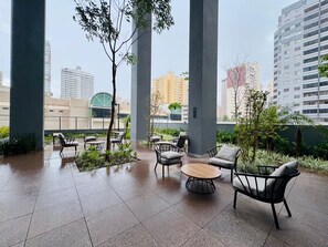 An outdoor seating area with chairs and a round table, surrounded by greenery and large pillars. - Apartment 3S across from the Shopping Center next to Vaca Brava Park (Goiânia)