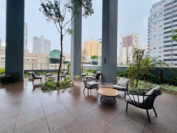 An outdoor seating area with chairs and a round table, surrounded by greenery and large pillars.