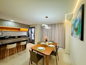Una cucina moderna con zona pranzo, che include un tavolo di legno apparecchiato per quattro persone, un lampadario a sospensione e un grande quadro astratto appeso al muro.