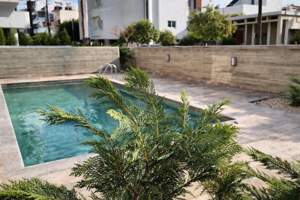 Una piscina con cubierta de madera, rodeada por un muro de ladrillo bajo y follaje.
