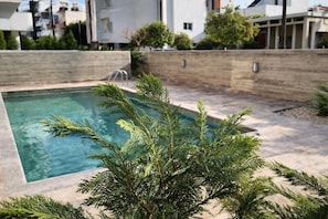 Ein Schwimmbecken mit Holzterrasse, umgeben von einer niedrigen Ziegelmauer und viel Grün.