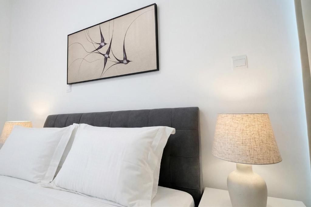 Una cama bien hecha con sábanas blancas, cabecera oscura y una obra de arte abstracta colgada en la pared.