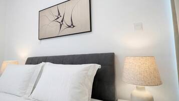 Una cama bien hecha con sábanas blancas, cabecera oscura y una obra de arte abstracta colgada en la pared.