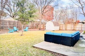 A backyard with a blue outdoor seating area, a small shed, and a wooden fence. - Backyard + Office + Clean + Comfy Beds (Fort Worth)